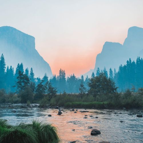 Serene river valley landscape with mountains and forests at sunrise, showcasing a tranquil natural environment ideal for eco-friendly outdoor activities and sustainable tourism.
